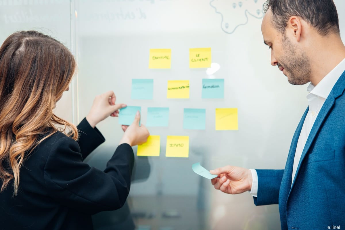 Deux conseillers We Invest construisent une stratégie ensemble devant un tableau de post-its