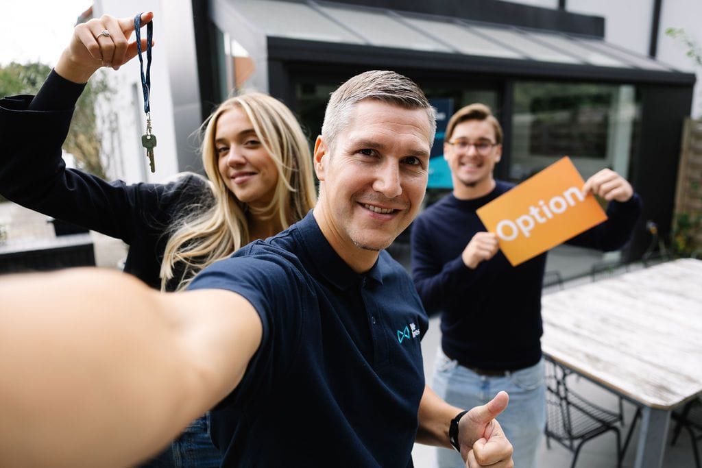 Un conseiller We Invest et ses clients, tout sourire, clés en main devant leur nouvelle maison