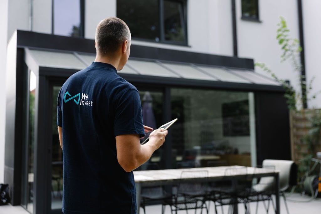 Un conseiller We Invest, tablette en main, devant une maison contemporaine